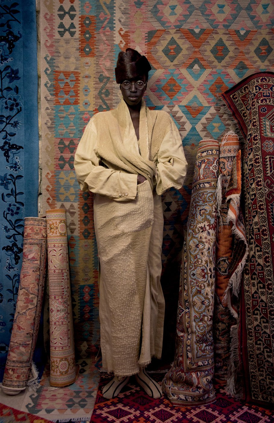 man stands in front of rolled up rugs 