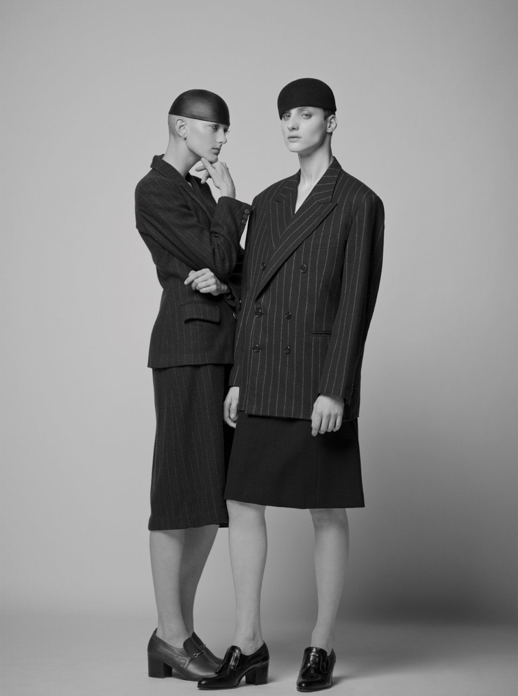 two people stand closely together, both wearing suit jackets and skirts