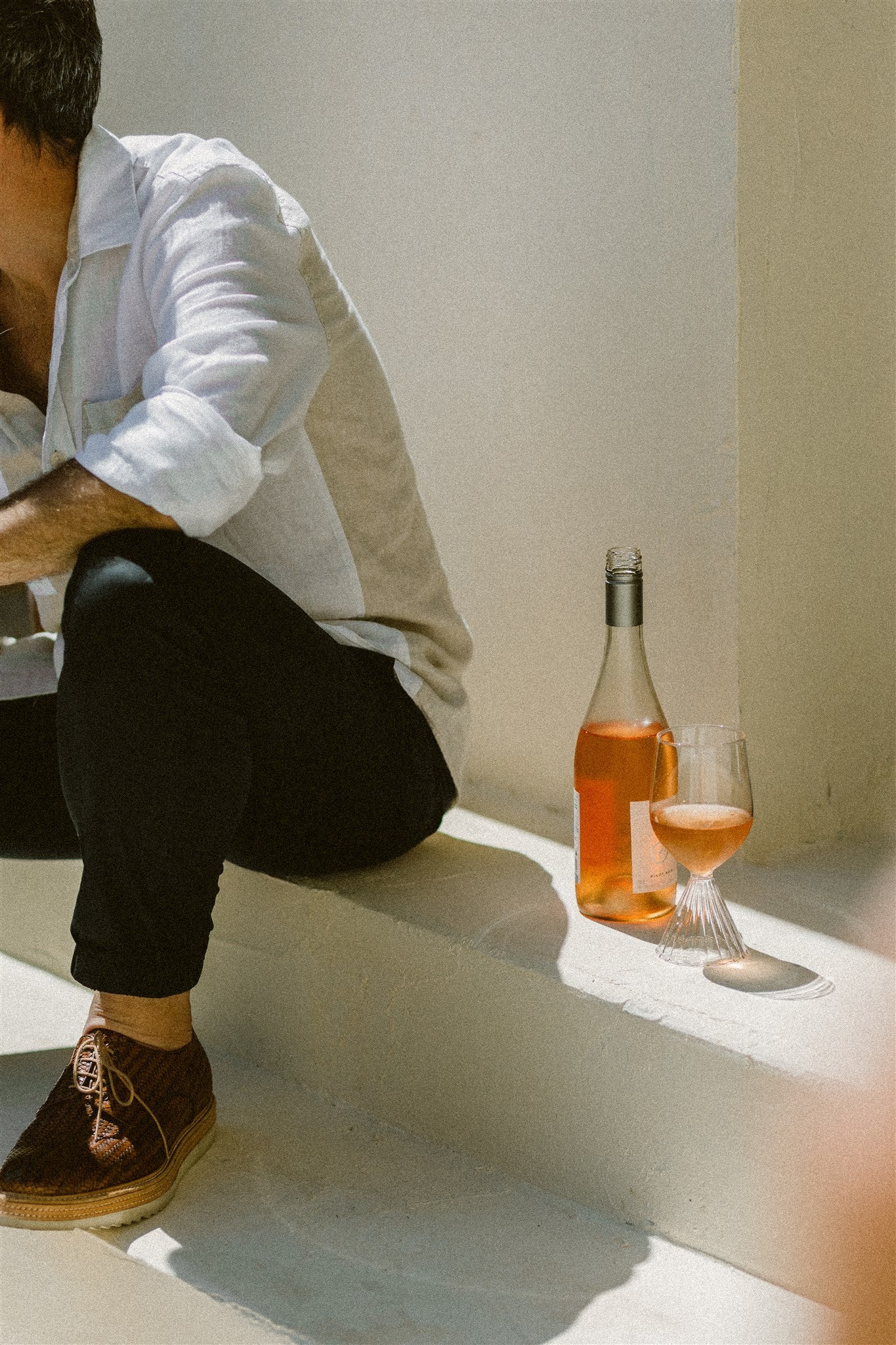 closeup of a bottle of rose and a glass of rose, placed on a sun drenched step