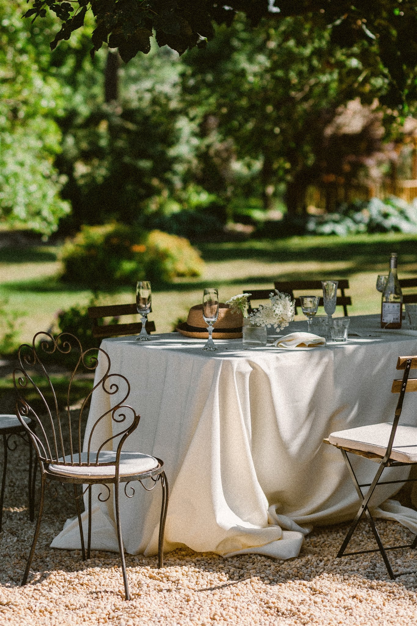 cast iron table and chairs sit outside, white tablecloth draped across table in the dappled light