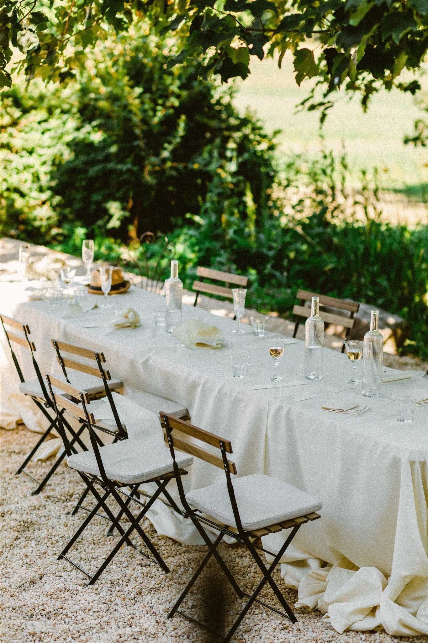 long table set with white tablecloth sits outside under a tree