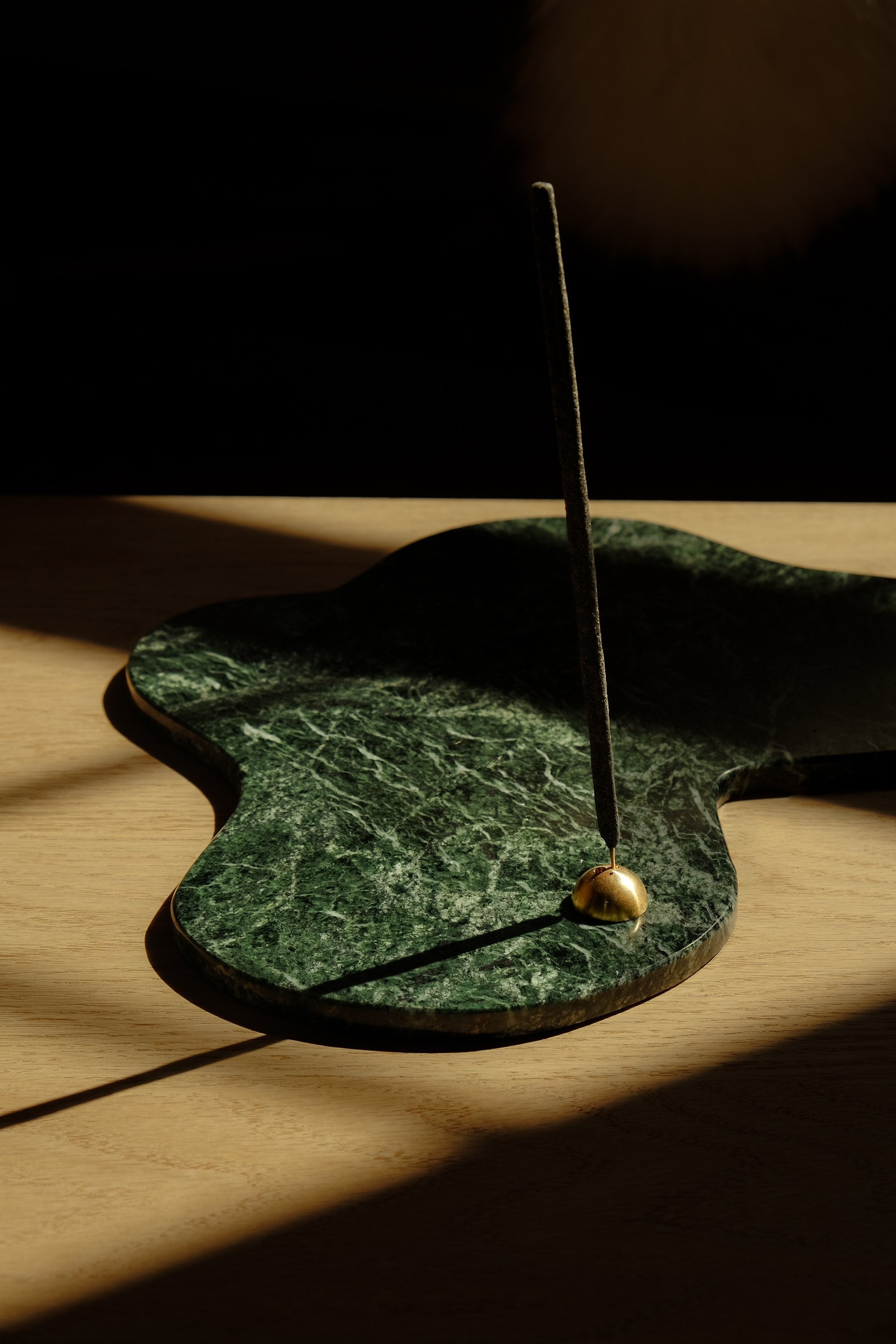 A minimalist half moon shape incense holder made of brass sitting on top of a green marble plate