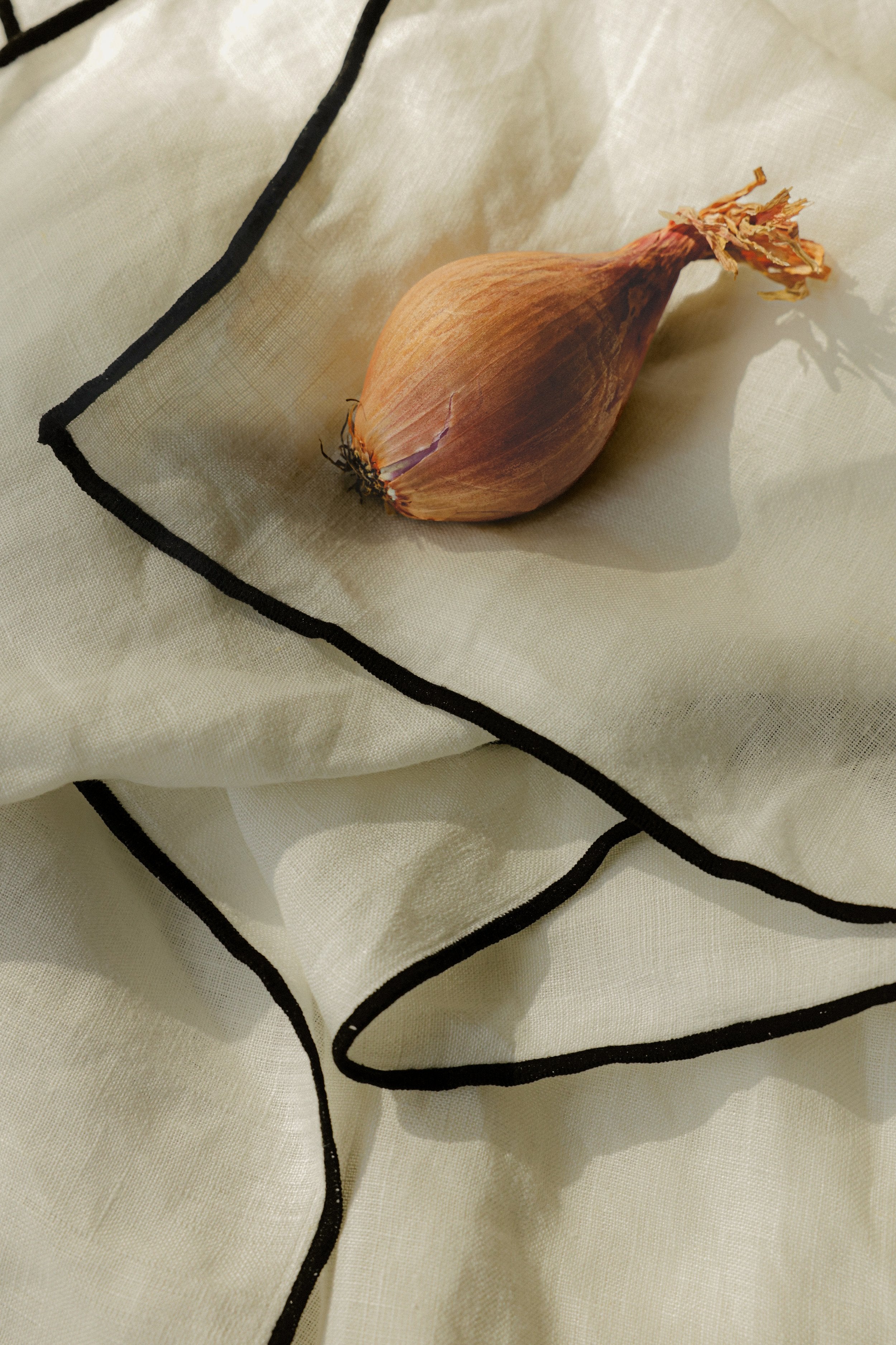 cream linen napkins with black edge detailing, a shallot sits on top