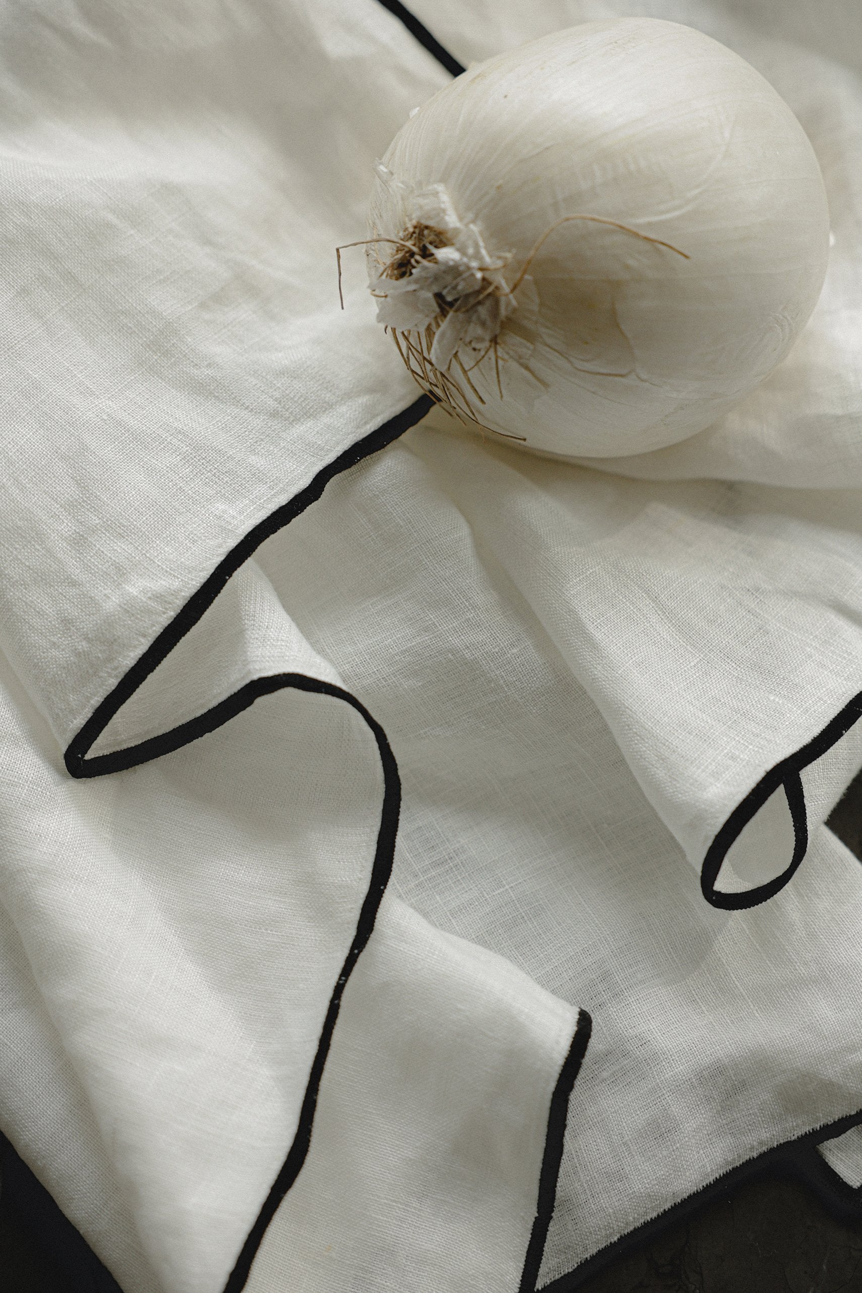 white linen napkins with black edge detailing, a white onion sits on top of the napkins