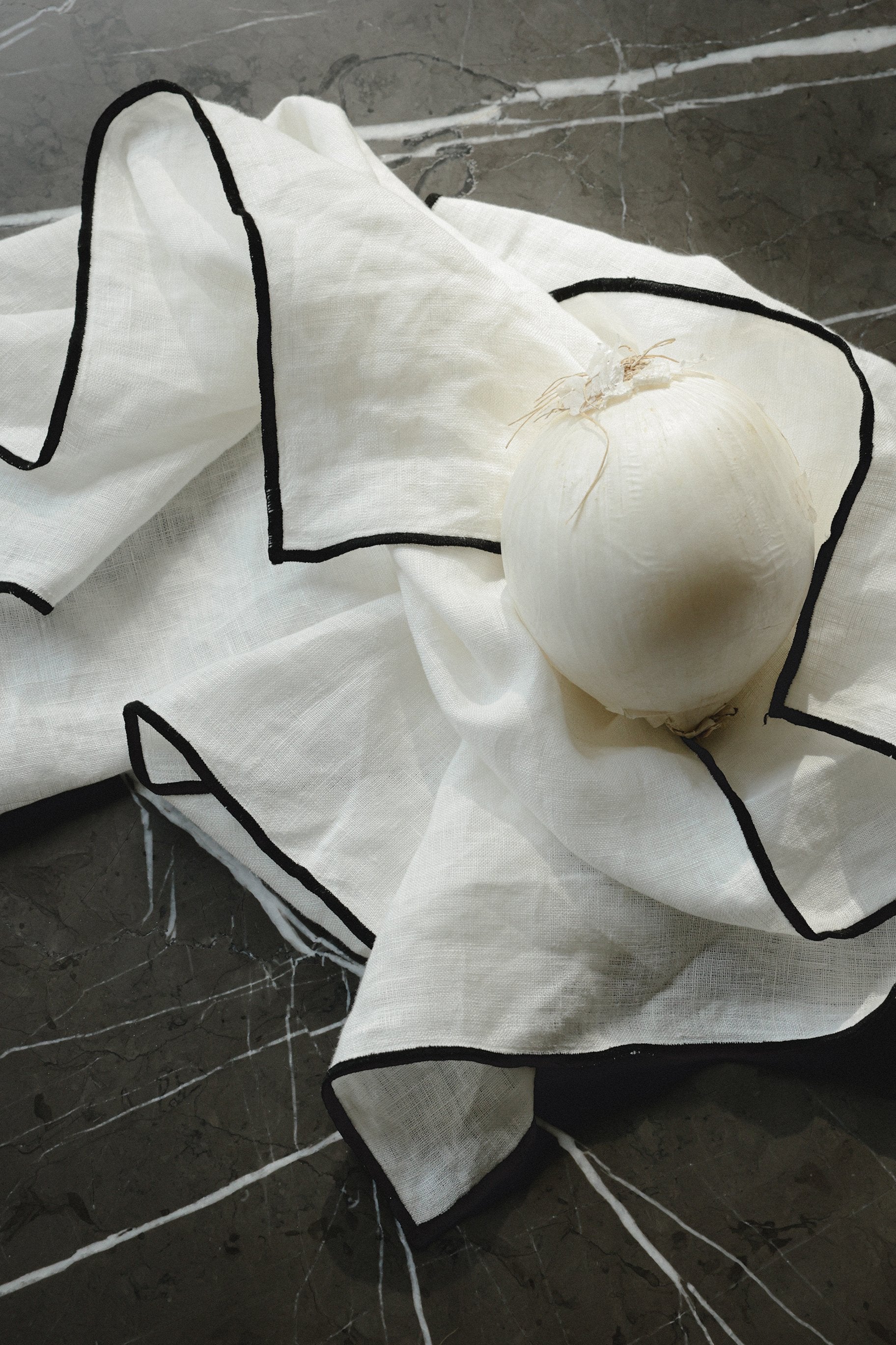 white linen napkins with black edge detailing, a white onion sits on top of the napkins