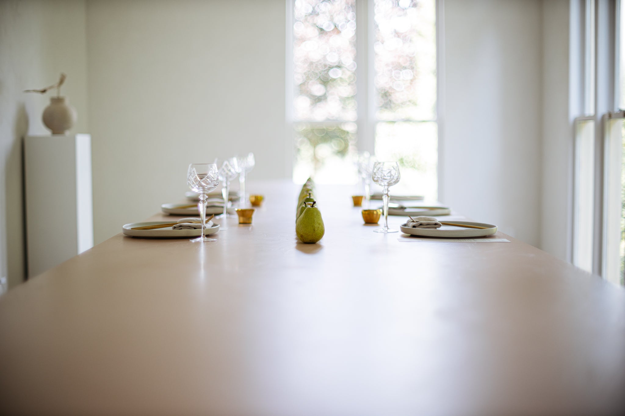 long table in a bright room set with place settings and a long row of pears down the middle