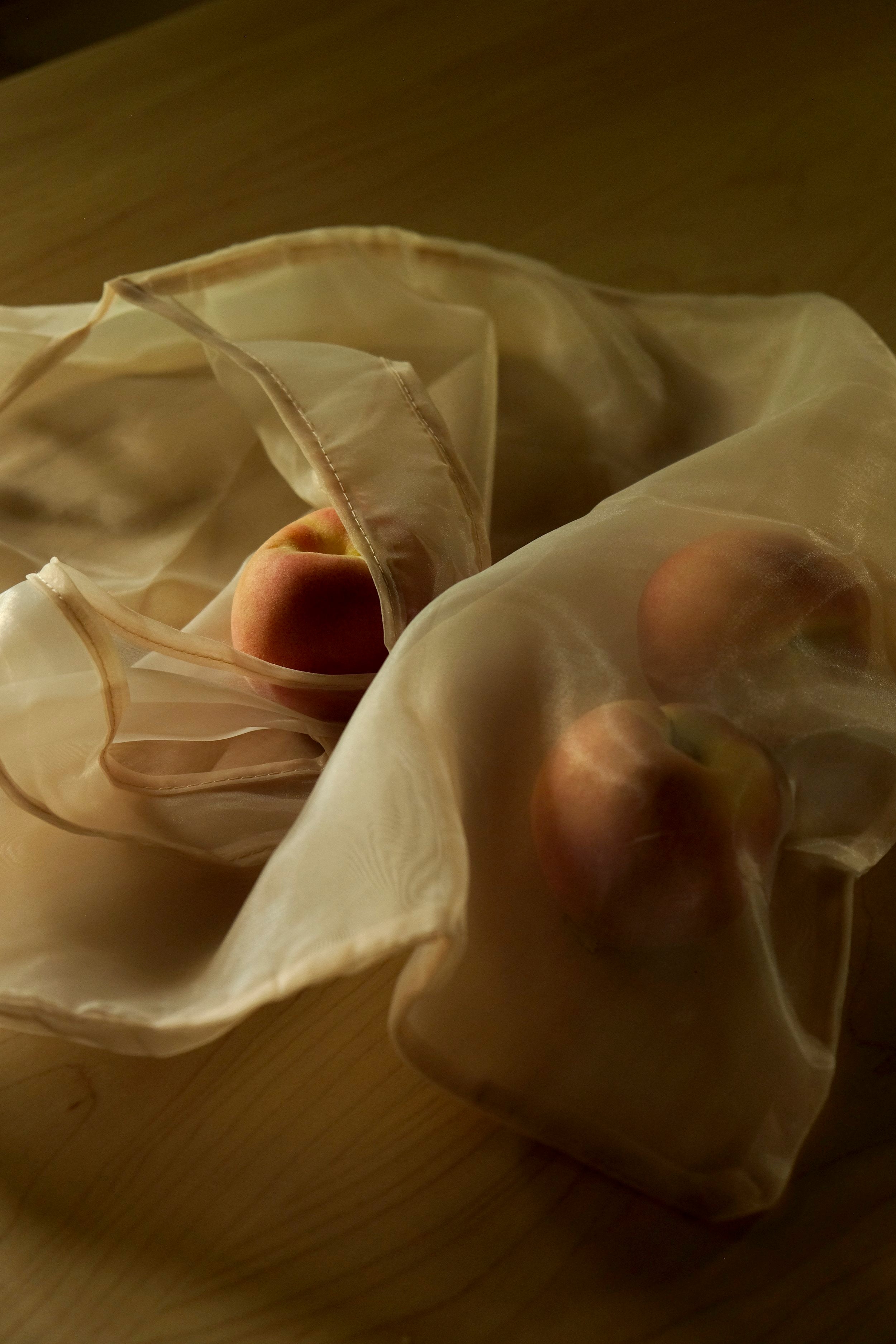 peaches sit on a table inside an organza tote