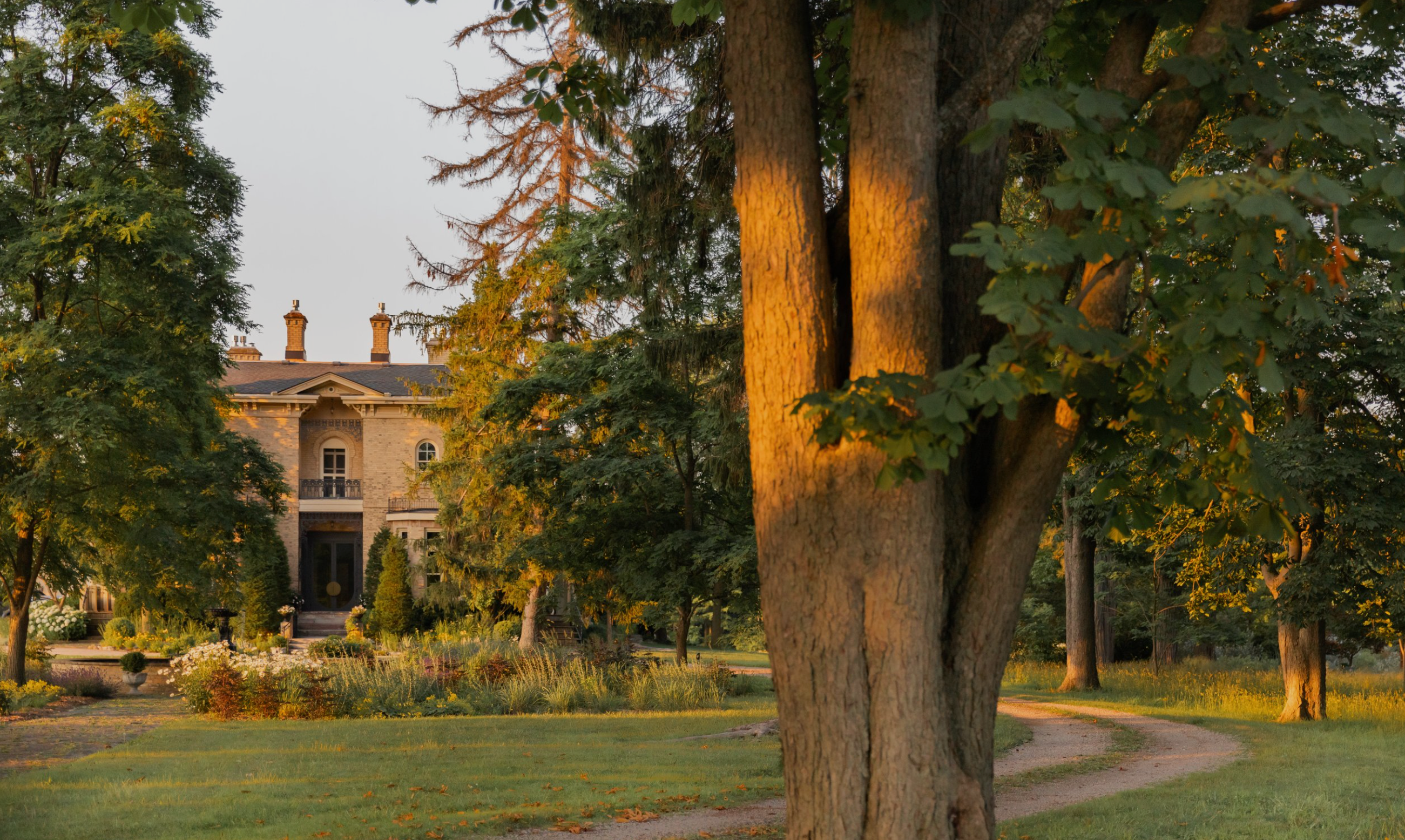 a yellow brick italian style manor, a lush garden and a long circular driveway