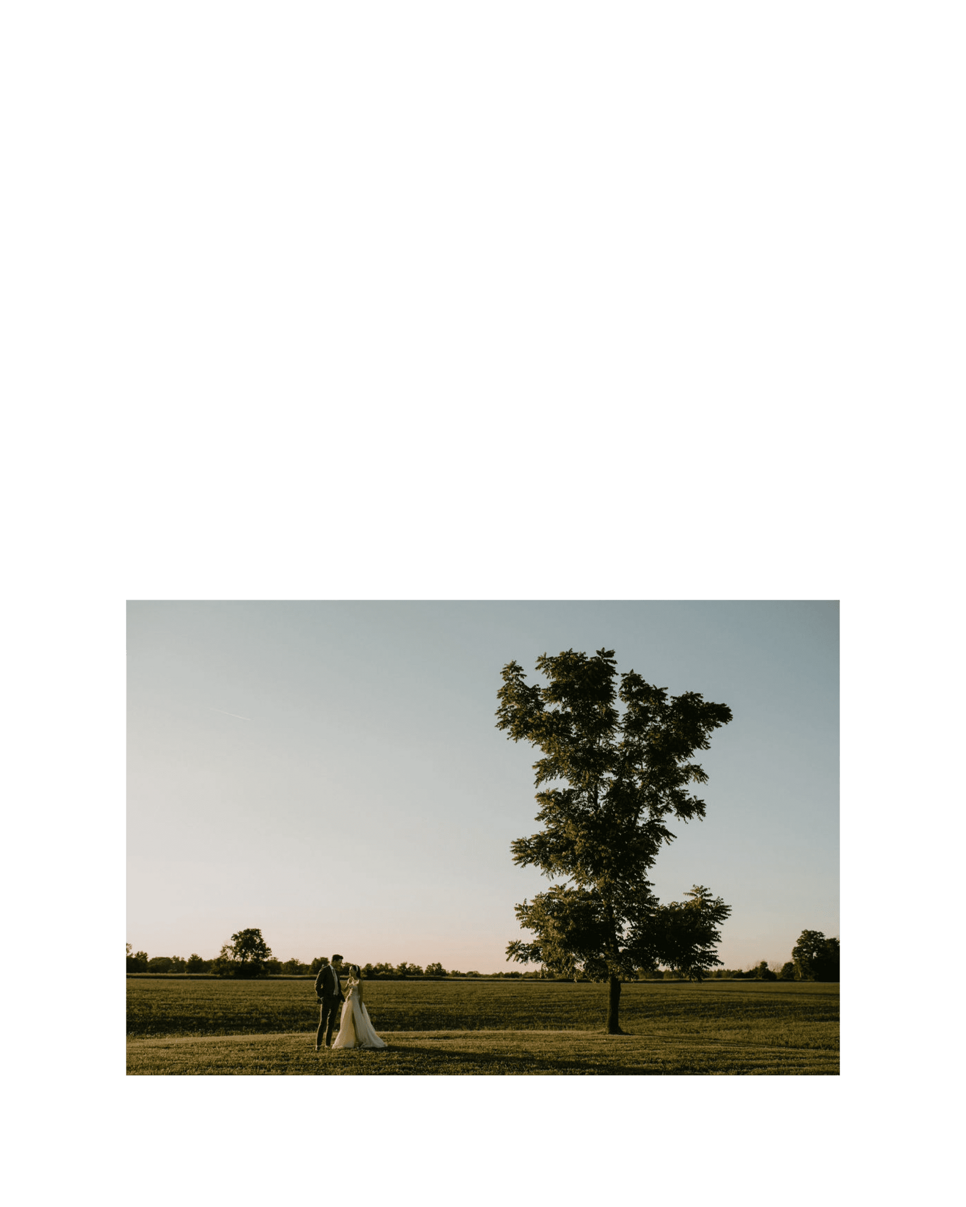 bride and groom stand together in front of large field